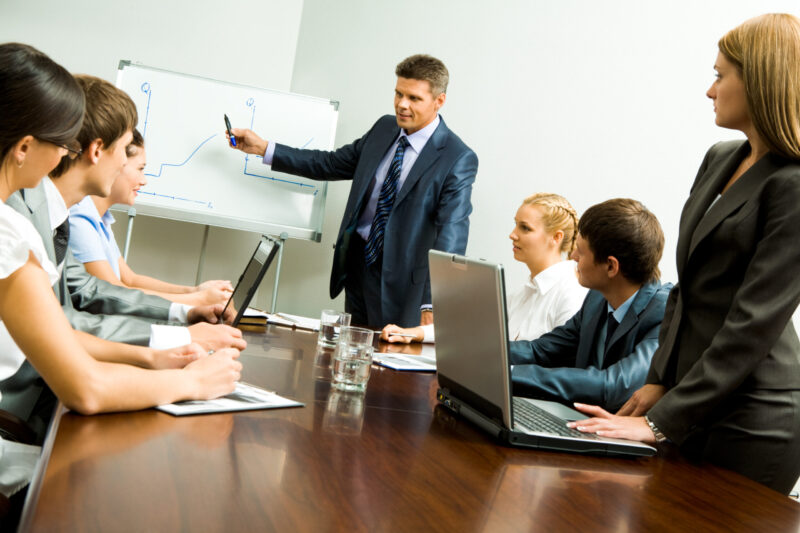Image of smart business people looking at their leader while he explaining something on whiteboard during seminar